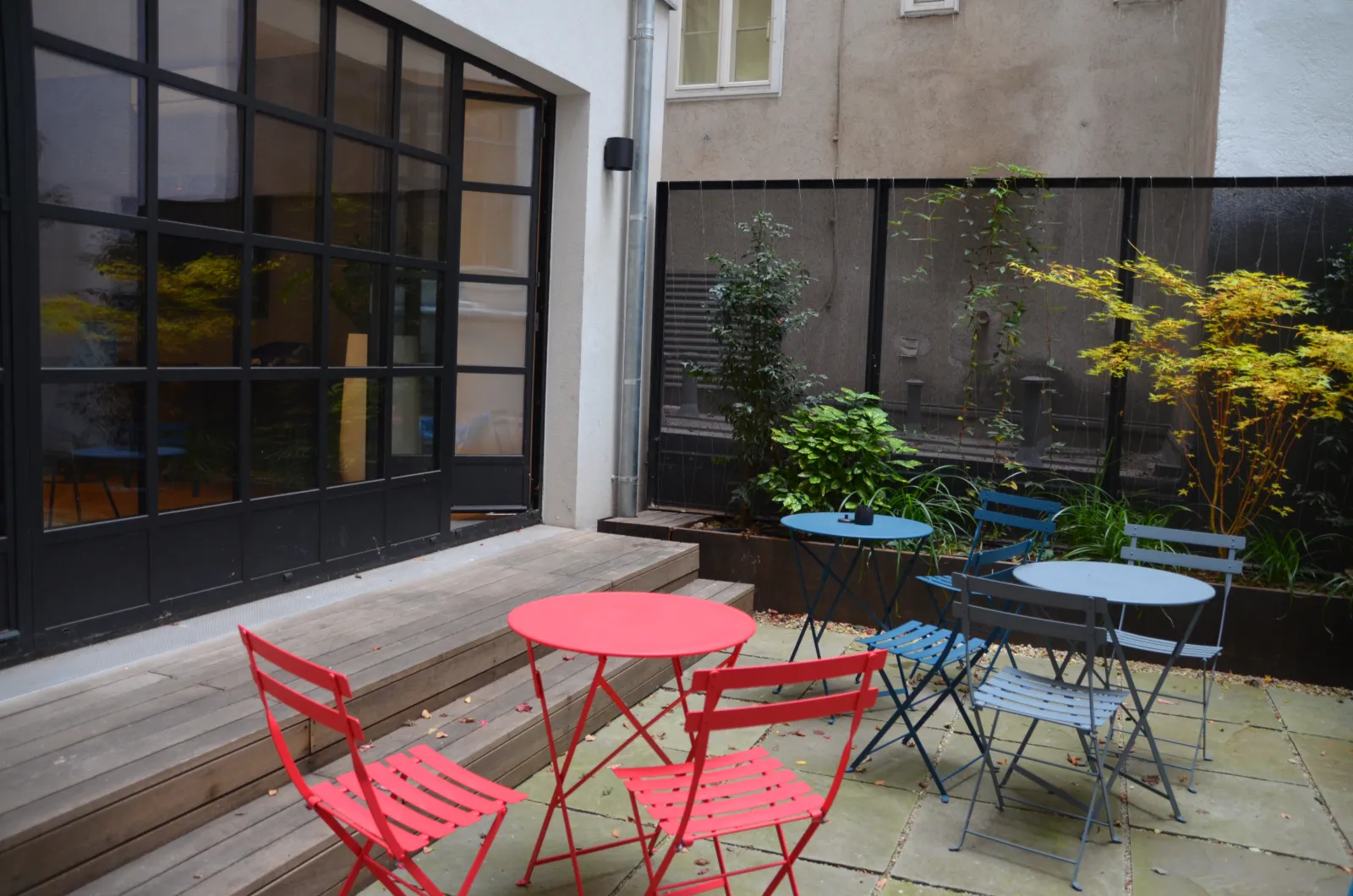 Der Innenhof von LOFT1080 bei Tag mit Bistromöbeln vor den Glasfenstern des Lofts