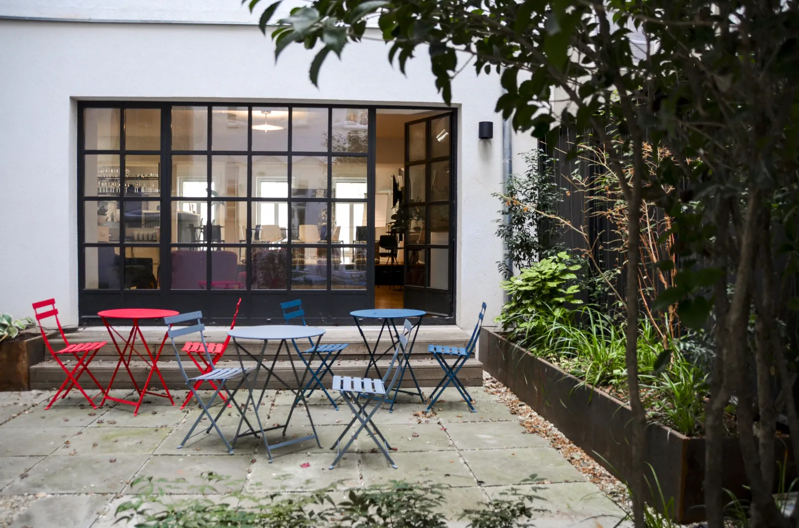 Innenhof im LOFT1080 mit roten und blauen Bistromöbeln auf Steinboden vor den Industrieglastüren
